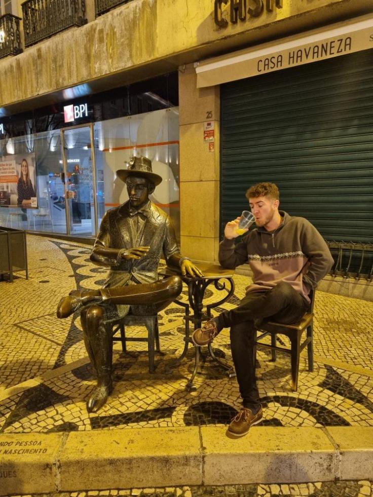 Calum sits drinking with a statue